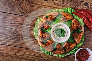 Delicious grilled chicken wings with garlic and tomato sauce with lettuce on a round board on wooden rustic background