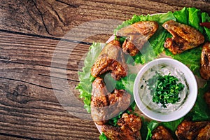 Delicious grilled chicken wings with garlic and tomato sauce with lettuce on a round board on wooden rustic background