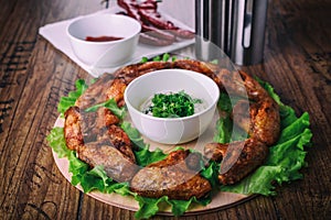 Delicious grilled chicken wings with garlic and tomato sauce with lettuce on a round board on wooden rustic background