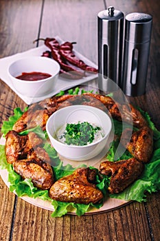 Delicious grilled chicken wings with garlic and tomato sauce with lettuce on a round board on wooden rustic background