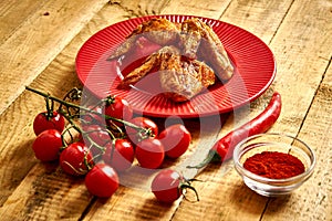 Delicious grilled chicken wings on red plate with spices and tomatoes and chilly peppers on table.