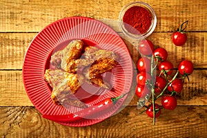 Delicious grilled chicken wings on red plate with spices and tomatoes and chilly peppers on table.