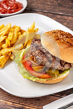 Delicious grilled homemade hamburger with beef, tomatoes, cheese, and lettuce on rustic wooden background