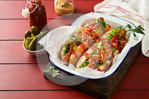 Delicious grilled hotdog with pickled cucumbers, chili peppers, caramelized onions, ketchup, mustard in craft paper on red old