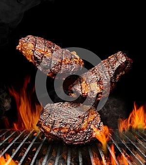 Delicious grilled pork or beef steaks are falling down on black background. Barbecue bbq grill, flaming fire, ember