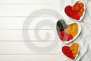 Delicious gummy fruit shaped candies on white wooden table, flat lay. Space for text