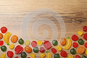 Delicious gummy fruit shaped candies on wooden table, flat lay. Space for text