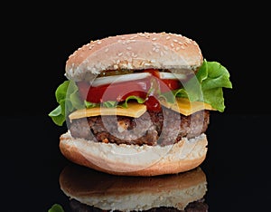 Delicious hamburger with beef with cheese, tomatoes, onions, cucumbers and tomatoes and ketchup on a black background and on a bla