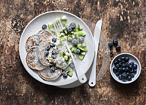 Delicious healthy breakfast - whole wheat pancakes with greek yogurt, blueberries, kiwi, honey and nuts on a wooden background, to