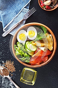 Delicious healthy brunch - boiled egg, smoked salmon, green salad and savory pancakes on a dark background, top view