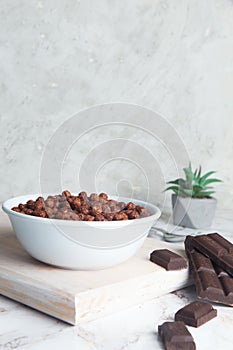 Delicious and healthy chocolate cereal in bowl with chocolate pieces laid down next to it