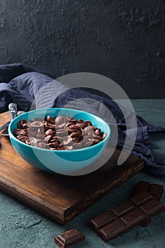 Delicious and healthy chocolate cereal in bowl with chocolate pieces laid down next to it