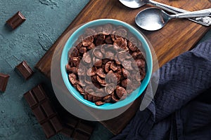 Delicious and healthy chocolate cereal in bowl with chocolate pieces laid down next to it