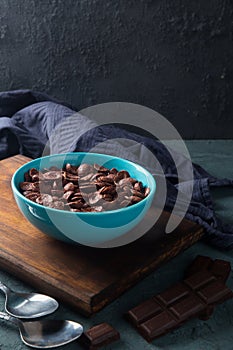 Delicious and healthy chocolate cereal in bowl with chocolate pieces laid down next to it