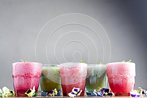 Delicious healthy kiwi and strawbeery, raspberry smoothies served with fresh mint in glasses on rustic wooden table.