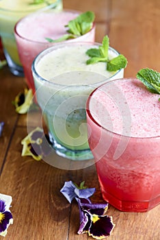 Delicious healthy kiwi and strawbeery, raspberry smoothies served with fresh mint in glasses on rustic wooden table.