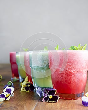 Delicious healthy kiwi and strawbeery, raspberry smoothies served with fresh mint in glasses on rustic wooden table.