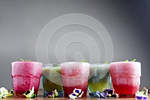 Delicious healthy kiwi and strawbeery, raspberry smoothies served with fresh mint in glasses on rustic wooden table.