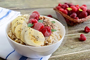 Delicious and healthy oatmeal with banana, raspberries, nuts.