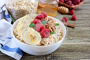 Delicious and healthy oatmeal with banana, raspberries, nuts.