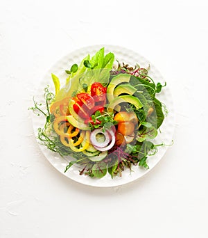 Delicious healthy salad of fresh avocado, tomatoes, cucumbers, peppers, lettuce, microgreens on white plate. Clean eating, lunch
