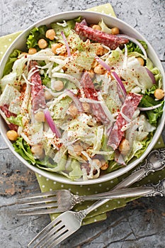 Delicious and healthy salad made with fresh ingredients such as lettuce, salami, mozzarella, and garbanzo beans topped with a photo