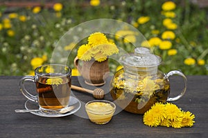 Delicious herbal tea made of fresh dandelion flowers with honey on wooden table in garden, close up