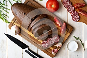 Delicious homemade bread cut into slices and a sausage sandwich on a wooden board. Top view
