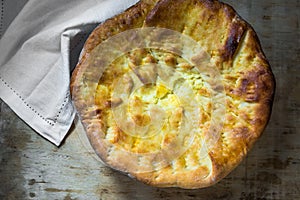 Delicious homemade cheese flat bread with golden crust on aged wood table, white napkin top view