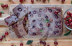 Chocolate sheet cake with sour cherries on wooden background