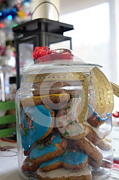Delicious homemade colourful christmas cookies in a handmade decorated jar and a candle and christmas tree in the back