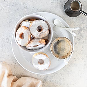 Delicious homemade donuts with sugar and a cup of coffee on a white stone background. square