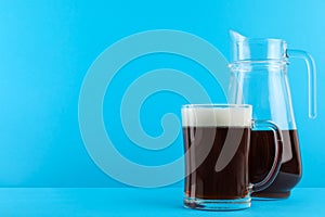 Delicious homemade kvass in glass mug and jug on blue background. Space for text
