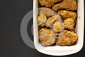 Delicious homemade oven baked fried chicken in a dish over black surface, top view. Flat lay, overhead, from above. Space for text