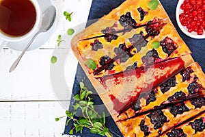 A delicious homemade pie with berries, cut into pieces and a cup of fragrant tea.