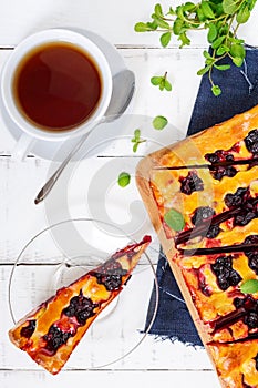 A delicious homemade pie with berries, cut into pieces and a cup of fragrant tea