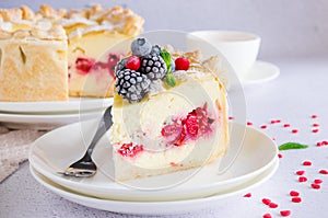 Delicious homemade puff pastry pie or cake with cream cheese filling and cherry on a white plate on a light stone background.