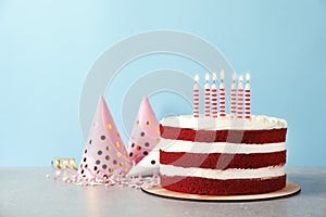 Delicious homemade red velvet cake with candles on table against color background.