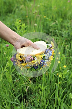 A delicious homemade sandwich with flowers on a background of green grass in the hand of a European girl. Creative