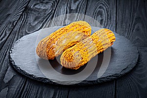 Delicious homemade sweet eclair on dark wooden background.