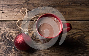 Delicious hot chocolate cocoa drink in red mug with christmas red ball on wooden background, traditional winter drink