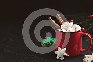 Delicious hot chocolate with marshmallows, cinnamon and gingerbread cookies on black table, space for text