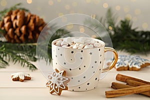 Delicious hot chocolate with marshmallows, gingerbread cookies and cinnamon on white wooden table against blurred festive lights