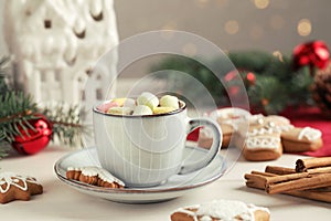 Delicious hot chocolate with marshmallows and gingerbread cookies on white wooden table against blurred festive lights