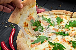Delicious hot pizza with salmon, arugula and different spices on wooden table ready to eat
