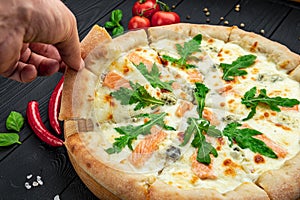 Delicious hot pizza with salmon, arugula and different spices on wooden table ready to eat