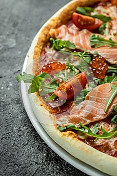 Delicious hot pizza with salmon, red caviar, tomatoes and aragula ready to eat. vertical image. top view. place for text