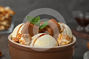 Delicious ice cream with caramel and popcorn in bowl on table