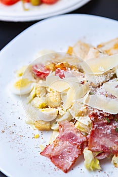 Delicious Italian caeasar salad with quali eggs,grilled bacon strips,parmesan cheese served on white plate in restaurant.Gourmet