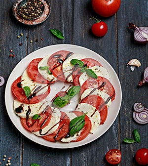 Delicious italian caprese salad with ripe tomatoes, fresh basil and mozzarella cheese on wooden rustic background. Italian caprese